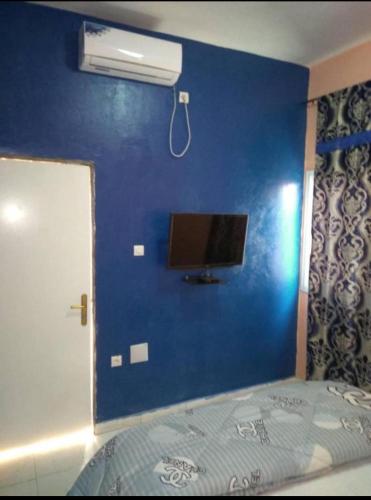 ein Schlafzimmer mit einer blauen Wand, einem TV und einem Bett in der Unterkunft Hotel Al Khayatt in Kaolack