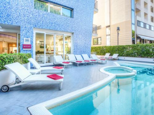 a swimming pool with lounge chairs and a building at Mercure Rimini Lungomare in Rimini