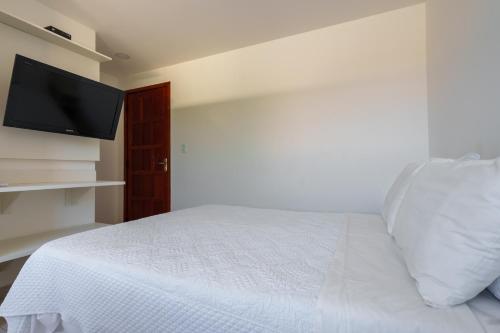 a bedroom with a white bed and a flat screen tv at Pousada do Timoneiro in Arraial do Cabo