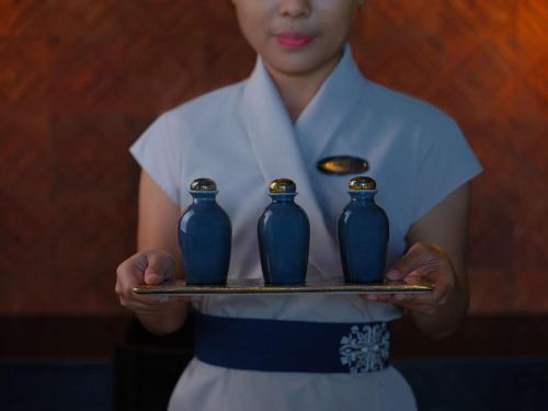 Uma mulher a segurar uma bandeja com três vasos azuis. em Raffles Bali em Jimbaran
