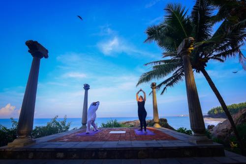 a group of three people doing yoga on the beach at Niraamaya Wellness Retreats, Surya Samudra, Kovalam in Kovalam