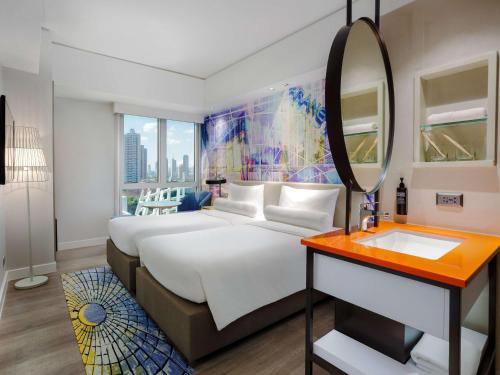 ibis Styles Manila Araneta City في مانيلا: غرفة نوم بسرير كبير ومرآة