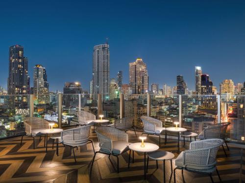 a rooftop bar with chairs and tables and a city skyline at Mercure Bangkok Surawong in Bangkok