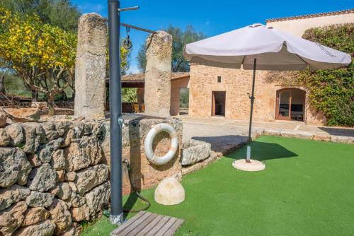 a stone wall with an umbrella and green grass at Can Pere Rapinya in Algaida