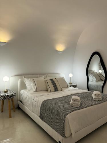 a white bedroom with a large bed and a mirror at Ater Albus Collection by K&K in Imerovigli