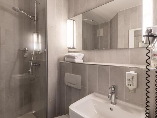 een badkamer met een wastafel, een douche en een spiegel bij B&B HOTEL Aachen City-Ost in Aken