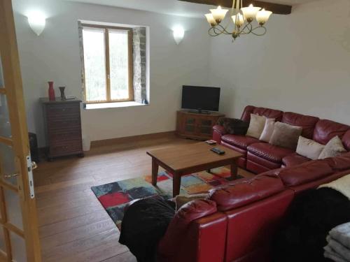 a living room with a red leather couch and a table at NormanD Holiday Home - VIRE CALVADOS Relaxing Rural Retreat in Le Reculey