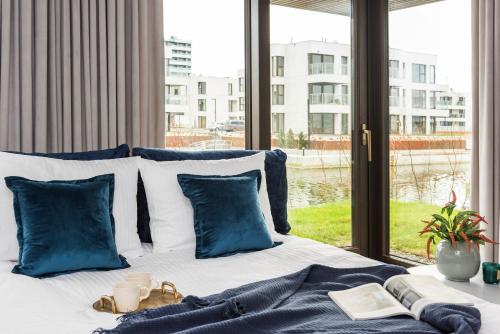a bed with blue and white pillows and a window at Sol Marina Resort Wyspa Sobieszewska II - LoftAffair Collection in Wiślinka