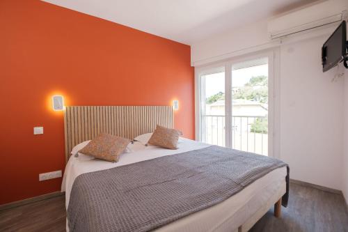 ein Schlafzimmer mit einem großen Bett und einer orangefarbenen Wand in der Unterkunft Anglade Hotel in Le Lavandou