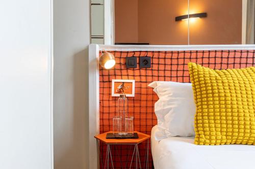 a bed with a yellow pillow and a lamp on a table at Hotel Olympic Paris Boulogne by Patrick Hayat in Boulogne-Billancourt