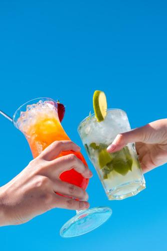 two woman hands holding two cocktails on a blue background at Onmood Cala Ratjada - Bed & Brunch in Cala Ratjada