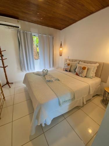 a bedroom with a large white bed with a window at Pousada Coco Dendê in Ilha de Boipeba