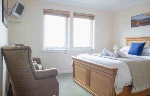 a bedroom with a bed and a chair and two windows at Solas Alainn in Staffin