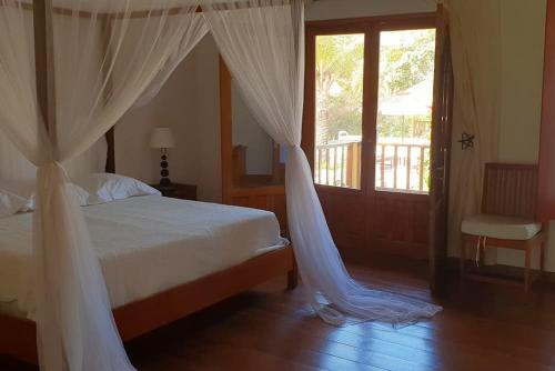 Schlafzimmer mit einem Bett mit weißen Vorhängen und einem Fenster in der Unterkunft Ocean Lodge Resort in Cap Skirring