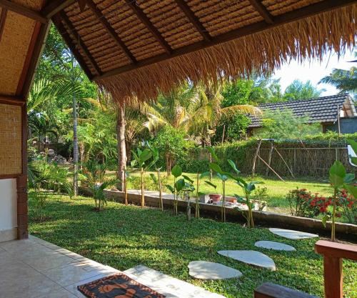 a patio with a grass roof and a garden at Bintang Tiga Bungalows Gili Air in Gili Air