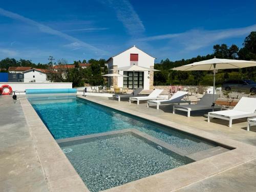 a swimming pool with chairs and an umbrella at Casa da Eira, Casaspensadas in Juncal