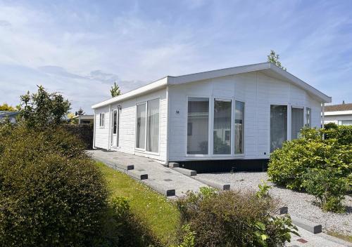 a white house with large windows in a yard at Chaletparc Krabbenkreek Zeeland - Chalet 84 in Sint Annaland