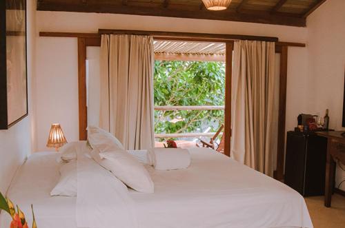 a white bed in a room with a window at Pousada Cores do Mar Caraíva in Caraíva