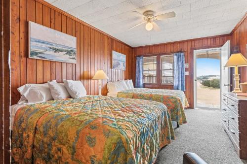 two beds in a room with wood paneled walls at Cavalier by the Sea in Kill Devil Hills