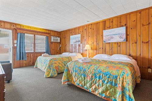 two beds in a room with wooden walls at Cavalier by the Sea in Kill Devil Hills