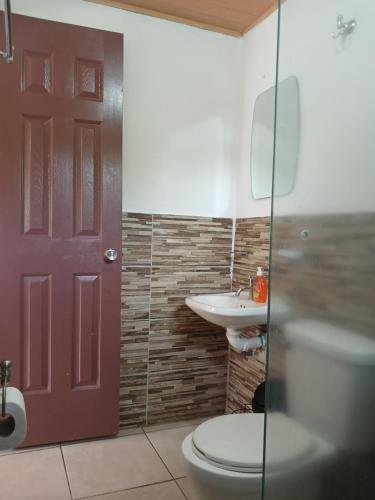 a bathroom with a toilet and a sink and a red door at Hotel Cabañas Casita La Ermita in San Carlos