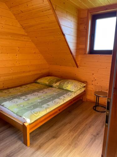 a bed in a wooden cabin with a window at Domki Za Górą in Jazowsko