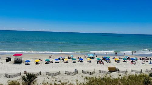 a group of people sitting on a beach with umbrellas at Ocean Reef- Unique Oceanfront Condo-Free parking - Amazing pools in Myrtle Beach