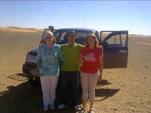 three people standing in front of a truck in the desert at GITE Take your time in Merzouga