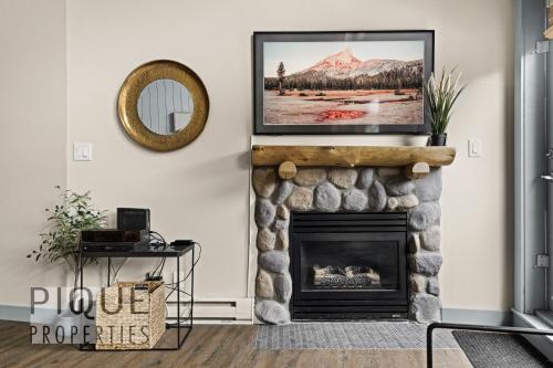 a living room with a fireplace with a picture on the wall at Mountain Loft Retreat, Heated Pool & Hot Tub, UG Parking, Balcony, WiFi! in Canmore