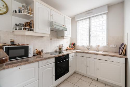 une cuisine avec des armoires blanches, un évier et un micro-ondes dans l'établissement Charmant appartement Villemomble, à Villemomble