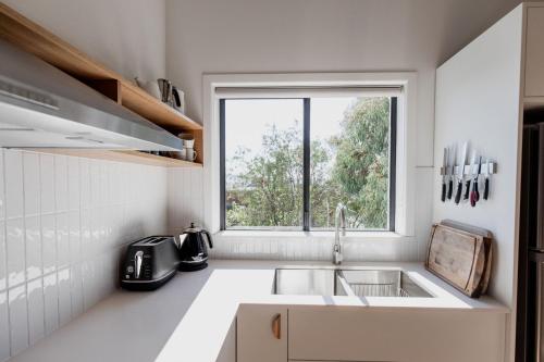 eine weiße Küche mit Spüle und Fenster in der Unterkunft Trendy apartment in the heart of West Hobart in Hobart