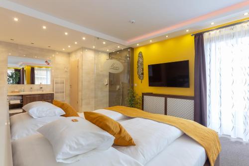 two beds in a bedroom with a tv and a bathroom at Hotel Mayer Alsóörs in Alsóörs