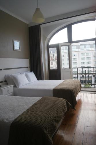 two beds in a hotel room with a large window at Hotel Chique Aliados in Porto