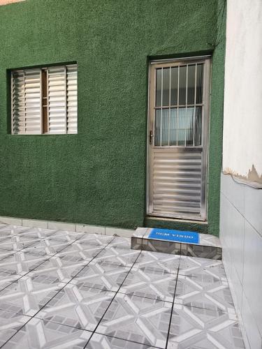 een groene muur met een deur en een tegelvloer voor een gebouw bij QUARTO ACONCHEGANTE in Guarulhos