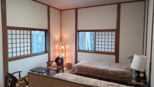 a bedroom with a bed and two windows and a chair at Forest Villa Shionine Kogen - Vacation STAY 45539v in Shiojiri