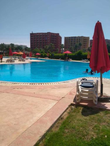 a swimming pool with a red umbrella and a white chair and an umbrella at بورتو جولف مارينا الساحل الشمالي 107 in Alexandria
