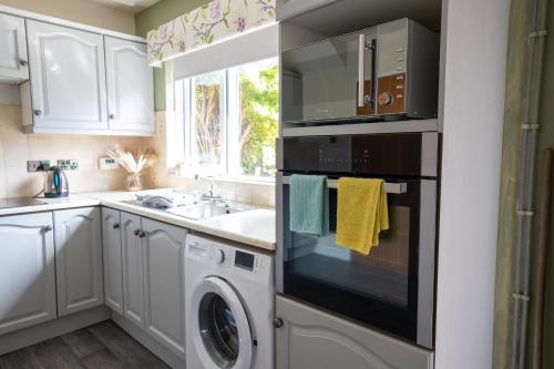 a kitchen with white cabinets and a washer and dryer at Golf Links Cottage - Views of Royal County Down in Newcastle