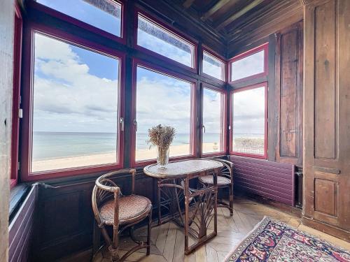 una mesa y sillas en una habitación con ventanas en Appartement exception avec vue sur mer imprenable, en Lion-sur-Mer
