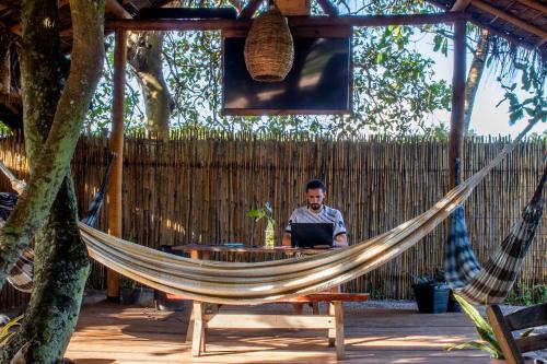 a man sitting in a hammock with a laptop at Padang Hostel in Pipa