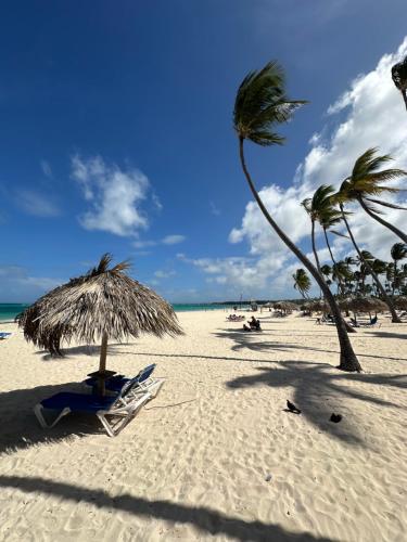 a beach with a straw umbrella and palm trees at punta beach bavaro hotel apartamentos in Punta Cana