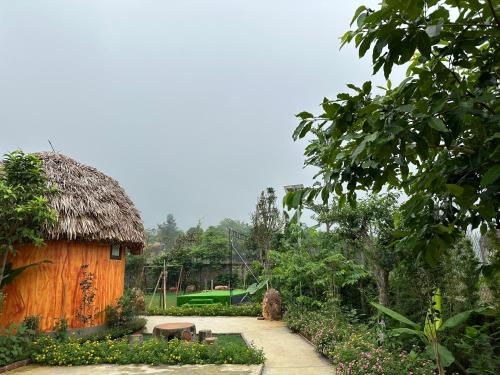 a hut with a thatched roof in a garden at King Bavi Resort in Ba Vì