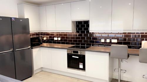 a kitchen with white cabinets and black appliances at The Lux Ville, Stunning 6 Bedroom Home in London in Plumstead