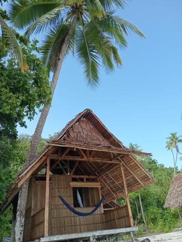 a hut on the beach with a palm tree at Nyande Rengkri Guest House in Kri