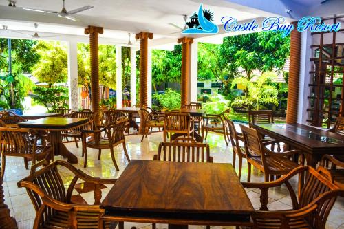 een restaurant met houten tafels, stoelen en ramen bij Castle Bay Resort in Weligama