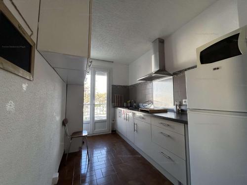 Elle comprend une petite cuisine avec des placards blancs et une fenêtre. dans l'établissement Appartement lumineux 3 pièces à 150m de la plage avec balcon et parking - Narbonne-Plage - FR-1-229B-101, à Narbonne