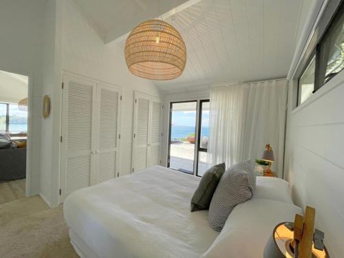 a white bedroom with a bed and a view of the ocean at Sea View Estate - Waiheke Escapes in Onetangi