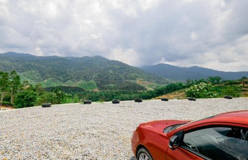 a red car parked on a gravel road with mountains in the background at Hillcrest Dawn, Bentong in Bentong