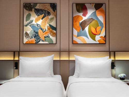 two beds in a hotel room with paintings on the wall at CLASSYC Hotel in Hanoi