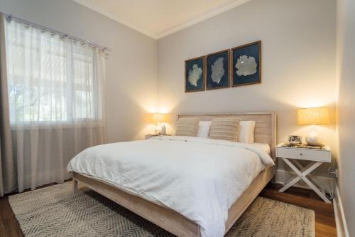 a white bedroom with a bed and a window at Belle Escapes - Moseley Apartments near the beach with private garden in Glenelg