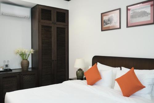 a bedroom with a bed with white sheets and orange pillows at Paul Chabot Hotel in Hai Phong